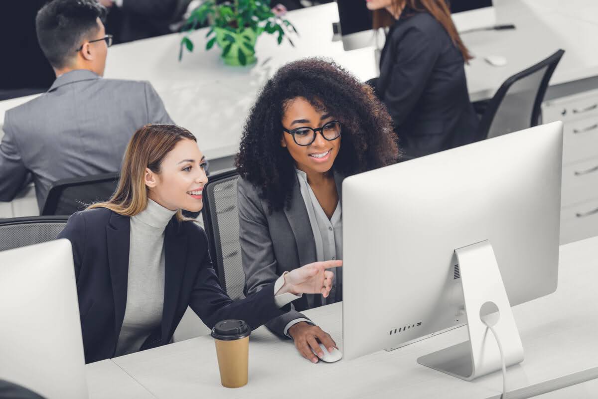 Two women look at a desktop computer screen in an office